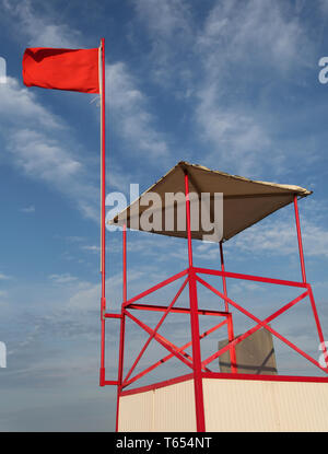 waving big red flag on the turret of lifeguard the in summer and blue sky on background Stock Photo
