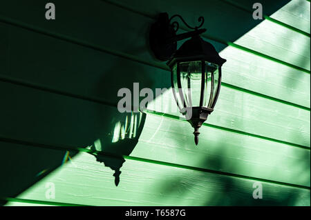 shadows and light - incandescent electric wall lamp on green wooden wall, lamp is off Stock Photo