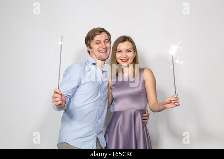 Party, celebration, event and holidays concept - man dressed in blue shirt and woman dressed in purple dress hold a firework stick Stock Photo
