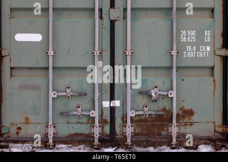 The doors of a large old container are painted in close-up in green with rust, with pipe-type locks and white lettering indicating its characteristics Stock Photo