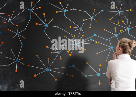 rear view of businesswoman looking at network structure or structure of social network on blackboard Stock Photo