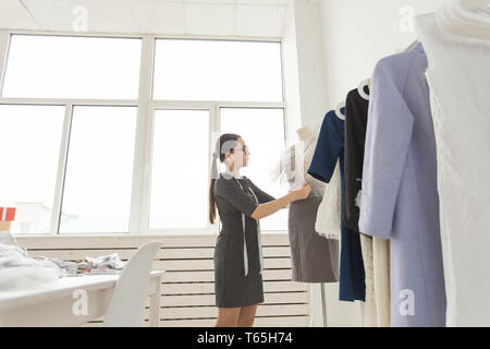 Dressmaker, fashion designer, tailor and people concept - designer dressed in stylish outfit measuring materials on mannequin Stock Photo
