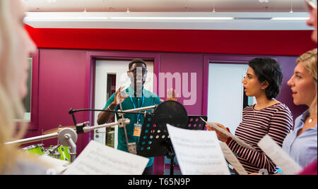 Male conductor leading women singing in music recording studio Stock Photo