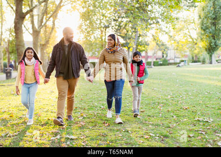 Muslim family holding hands, walking in sunny autumn park Stock Photo