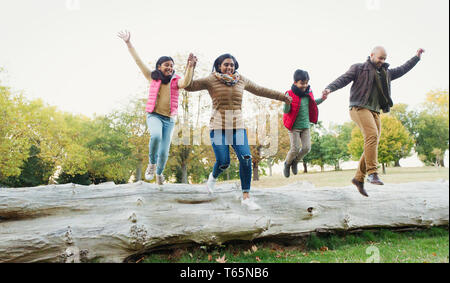 Happy, playful family holding hands, jumping off log in autumn park Stock Photo