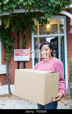 Portrait happy, confident woman moving house, carrying cardboard box in driveway Stock Photo