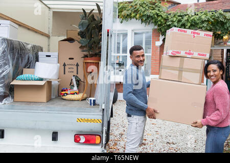 Portrait happy couple moving house, unloading cardboard boxes from moving van Stock Photo