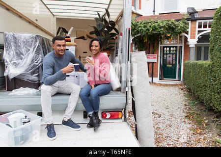 Portrait happy couple drinking tea, taking a break from moving at back of moving van Stock Photo