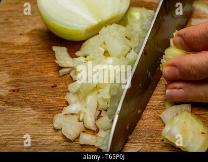 Close up of a chef dicing peeled organic brown onions (allium) with a sharp knife on a wooden chopping board. Stock Photo