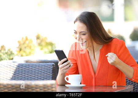 Excited woman checking smart phone content sitting in a coffee shop terrace Stock Photo