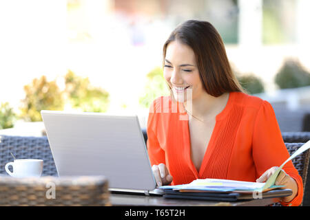 Happy entrepreneur working online with a laptop and documents sitting in a coffee shop Stock Photo
