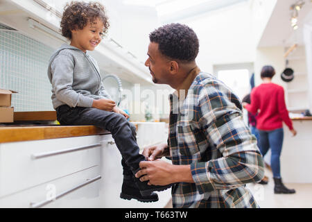 Father tying sons shoelace in kitchen Stock Photo