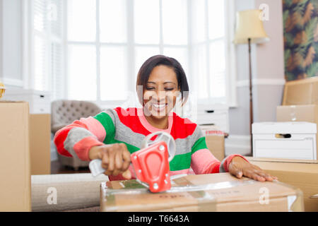 Smiling woman taping moving boxes, moving house Stock Photo