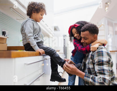 Father tying sons shoe in kitchen Stock Photo