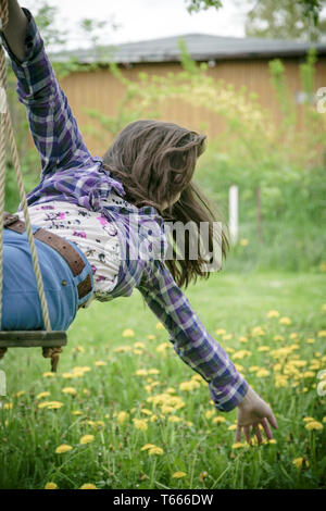 girl on a swing stretching here arm to a meadow Stock Photo