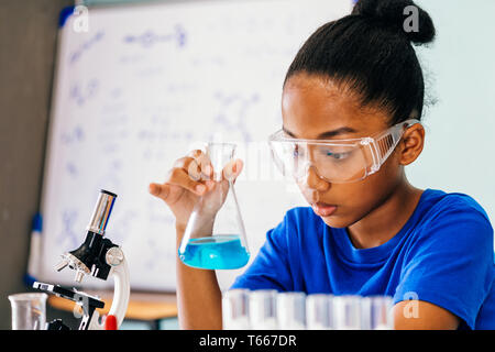 Young African American mixed kid testing chemistry lab experiment and shaking glass tube flask along with microscope - science and education concept Stock Photo