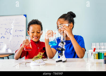 Two African American mixed kids tests chemistry lab and holding glass tube flask with microscope and smile in science classroom - fun learning concept Stock Photo