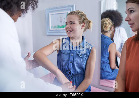Female pediatrician examining arm of girl patient in clinic examination room Stock Photo