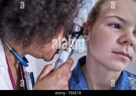 Close up female pediatrician using otoscope, examining ear of girl patient Stock Photo