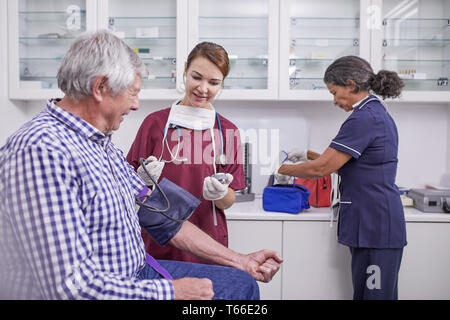 Female nurse checking blood pressure of senior male patient in clinic examination room Stock Photo