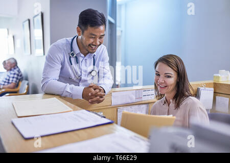 Smiling doctor and receptionist discussing medical record in clinic Stock Photo