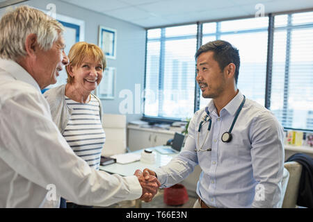 Male doctor shaking hands with senior couple in clinic doctors office Stock Photo