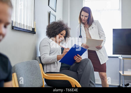 Female doctor and patient discussing paperwork in clinic waiting room Stock Photo