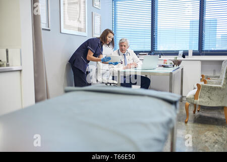 Doctor and nurse using digital tablet, consulting in clinic doctors office Stock Photo