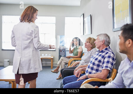 Female doctor talking with patients waiting in clinic waiting room Stock Photo