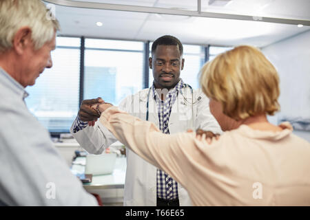 Male doctor examining senior patients shoulder in clinic examination room Stock Photo