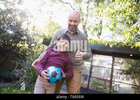 Father and son playing with soccer ball in backyard Stock Photo