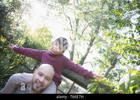 Portrait playful father carrying son on shoulders in backyard Stock Photo