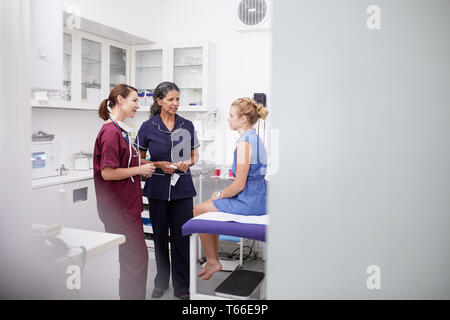 Female doctor and nurse talking to girl patient in clinic examination room Stock Photo