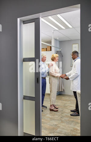 Doctor shaking hands with senior couple in clinic examination room