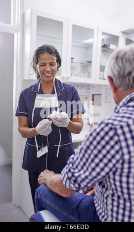 Female doctor taking blood from senior male patient in clinic examination room Stock Photo