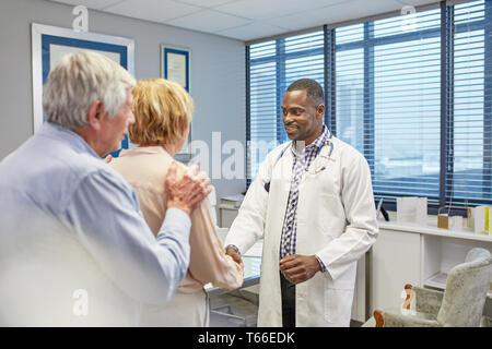 Doctor shaking hands with senior couple in doctors office Stock Photo