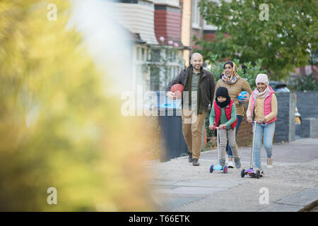 Muslim family walking and riding scooters on neighborhood sidewalk Stock Photo