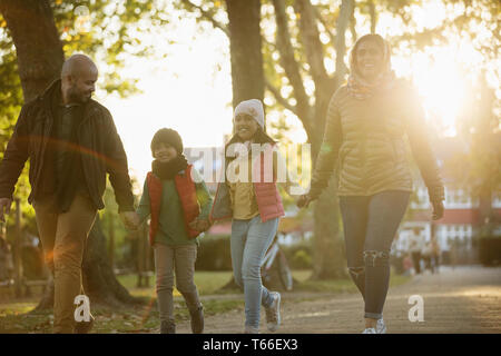 Happy family holding hands, walking in sunny autumn park