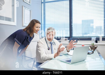 Doctor and nurse talking at laptop in doctors office Stock Photo