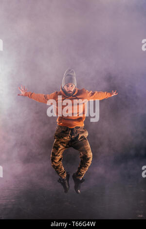 Male breakdancer jumps off high in the air while performing a cool dance move, a lot of smoke in the background. Stock Photo