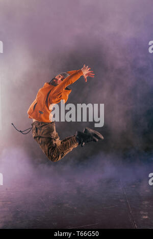 Male breakdancer jumps off high in the air while performing a cool dance move, a lot of smoke in the background. Stock Photo