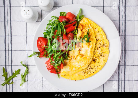 Classic omelet with cheese and tomatoes salad on a white plate. Stock Photo