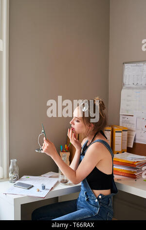 Young woman applying lip gloss in mirror Stock Photo
