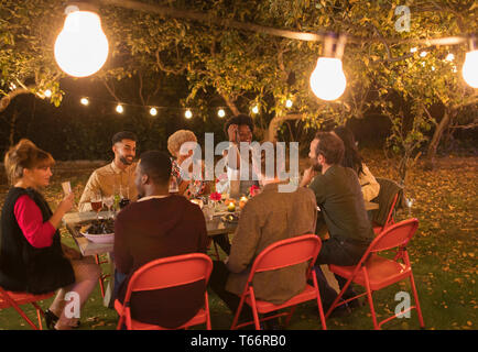 Friends enjoying dinner garden party under trees with fairy lights Stock Photo