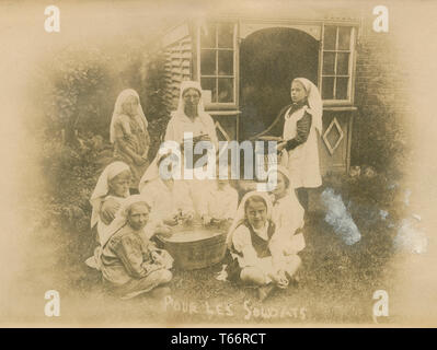 Antique c1919 postcard, “Pour les soldats,” showing a group of women and children sewing small pillows for the soldiers in France. Original caption: “Saturday afternoon war workers class…cutting up bits and filling limb pillows.” SOURCE: ORIGINAL PHOTOGRAPHIC POSTCARD Stock Photo