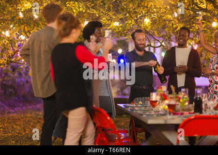 Friends celebrating, opening champagne at dinner garden party Stock Photo