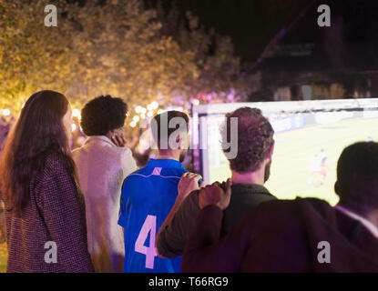 Friends watching soccer match on projection screen in backyard Stock Photo