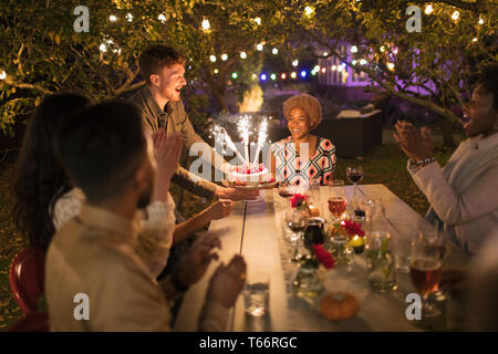 Happy friends celebrating birthday with sparkler cake at garden party table Stock Photo