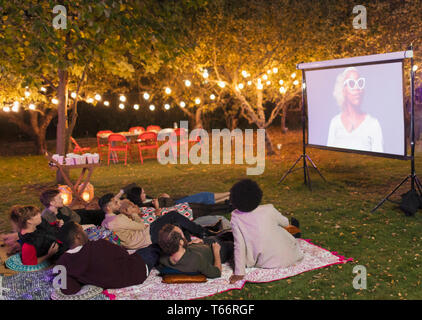 Friends watching movie on projection screen in backyard Stock Photo