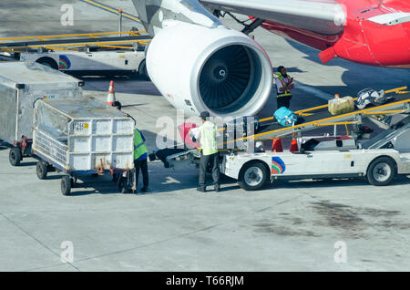 Bali, Denpasar, 2018-05-01: Man puts luggage from trailer to the conveyor belt on the plane. Unloading passenger baggage from airplane. Stock Photo
